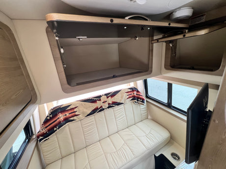 Inside an RV rental: a plush cream sofa with a Southwestern blanket, open overhead storage, and a TV for relaxation.