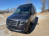 A dark gray Mercedes-Benz Sprinter van, perfect for an RV rental adventure, parked on a sandy lakeside area.