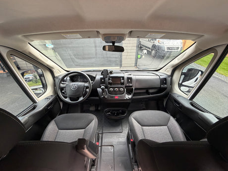 Inside an RV rental camper van: front cabin showing dashboard, steering wheel, seats, and outside view through the windshield.