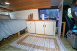 Custom RV rental interior: a cozy bed, compact kitchen with sink, and cabinet storage, perfect for mobile living.