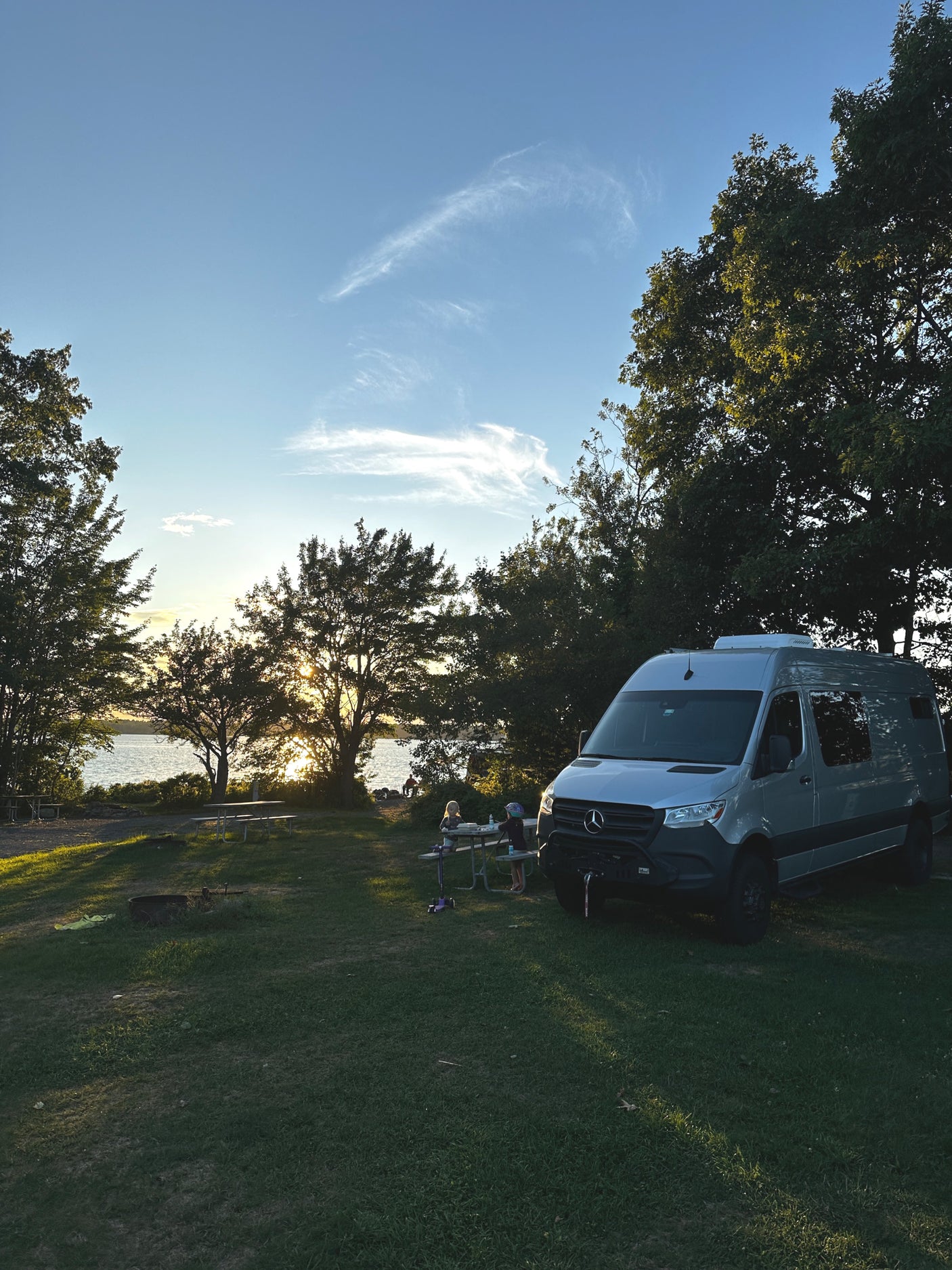 Enjoying an RV rental adventure: a gray camper van parked at a beautiful lakeside campsite during sunset with kids.