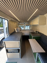 Step inside this modern RV rental: a compact living space with a bed, kitchen, custom storage, and stylish wood accents.