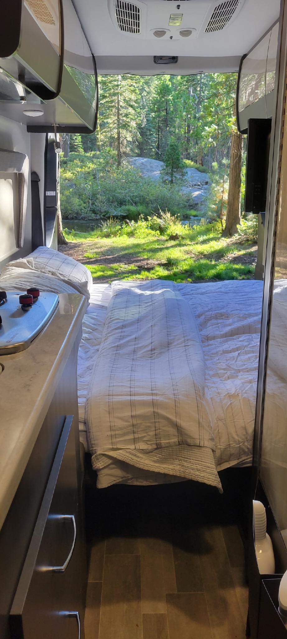 Cozy rv rental interior with a bed looking out onto a stunning forest and stream view. Perfect for nature lovers.