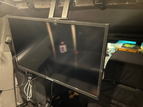 Inside an RV rental, a flat-screen TV is ceiling-mounted for mobile entertainment. Wires are visible, providing road trip viewing.