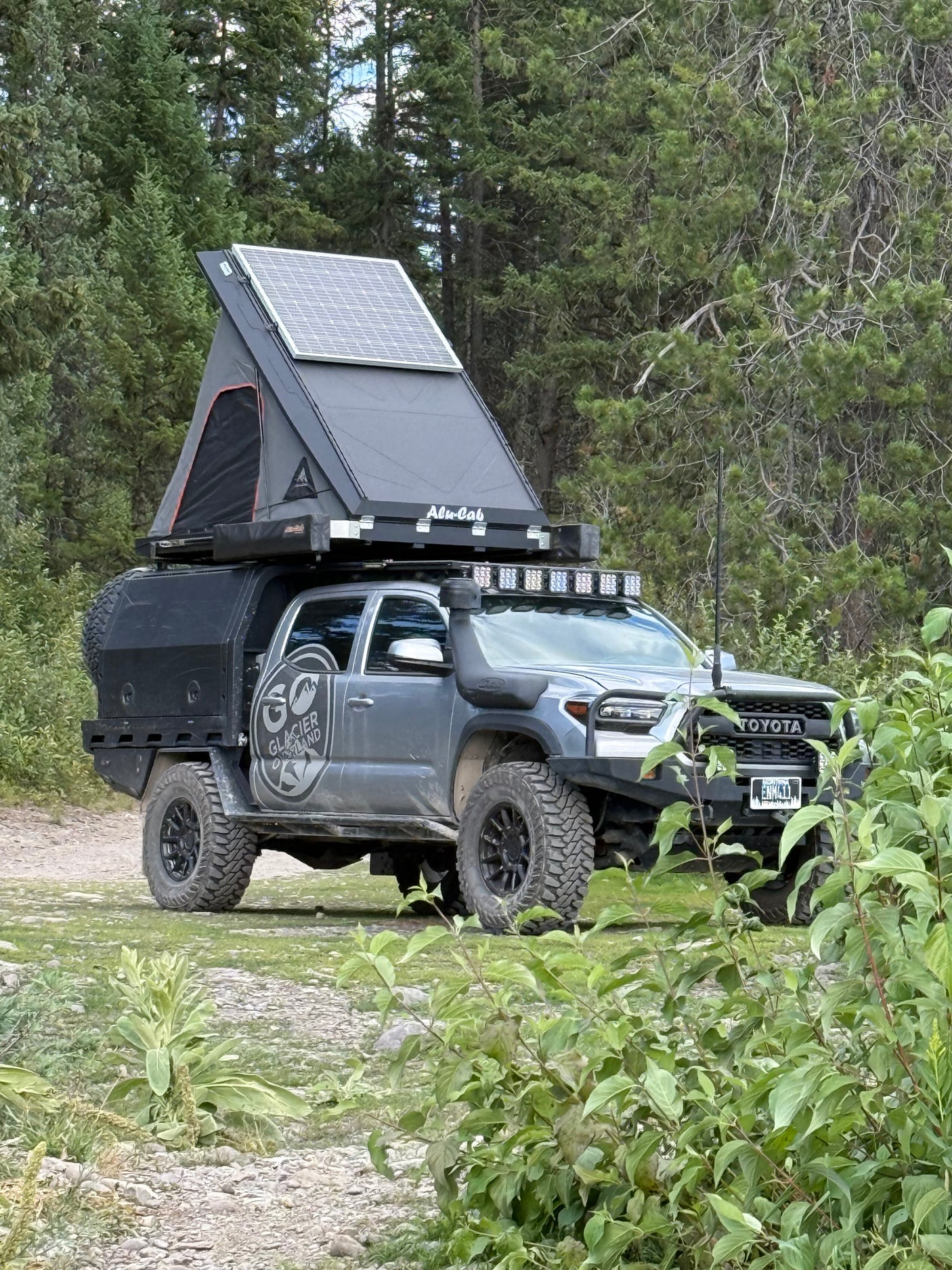 Grey Toyota Tacoma overlanding truck with rooftop tent, solar panel, and off-road gear. Ideal for your next rv rental adventure.