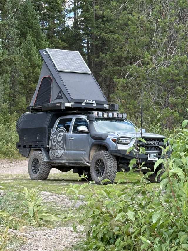 Grey Toyota Tacoma overlanding truck with rooftop tent, solar panel, and off-road gear. Ideal for your next rv rental adventure.