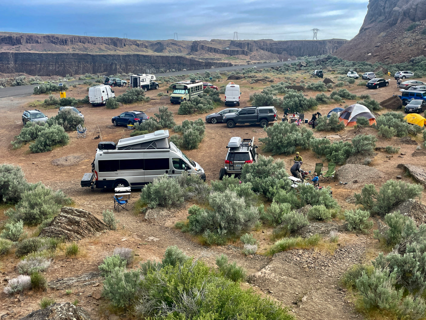 RV rental enthusiasts gathered! Vans, campers, and tents spread across a rugged desert canyon for dispersed camping.