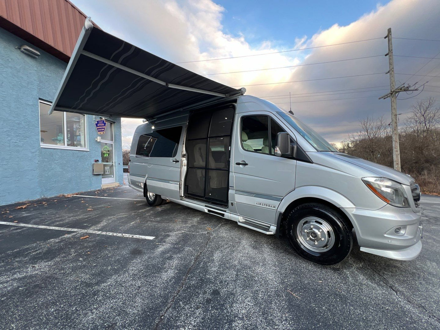 Silver Airstream camper van with awning extended, parked by a blue building. Your ideal rv rental.