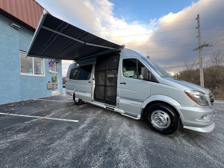 Silver Airstream camper van with awning extended, parked by a blue building. Your ideal rv rental.