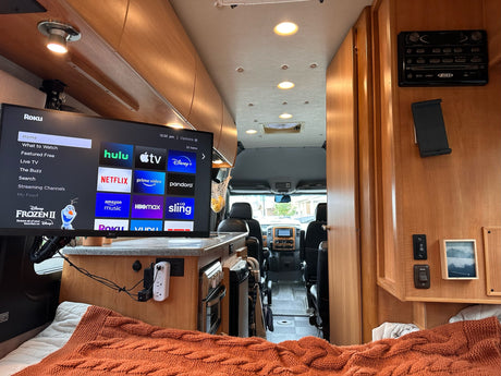 Cozy rv rental interior with a large Roku TV, comfy bed, and compact kitchen area. Ready for adventures.