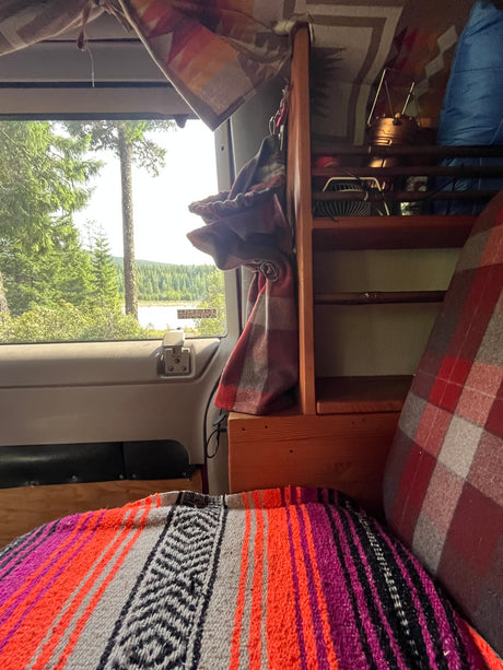 Cozy rv rental interior with vibrant blanket, wooden shelves, and a serene lake and forest view.