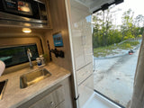 Compact RV rental kitchen area features a microwave, sink, and wood-grain cabinets. Perfect for mobile living.