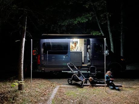 Nighttime fun with an RV rental: lit camper van with person at kitchen, and kids playing by stroller outside.