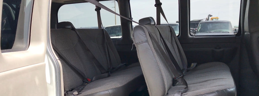 Inside an RV rental van showing worn grey passenger seats with seatbelts. View of other vehicles outside.