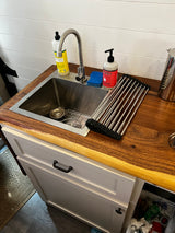 Inside an RV rental, a clean kitchen sink area with a wood counter, soap, and drying rack.
