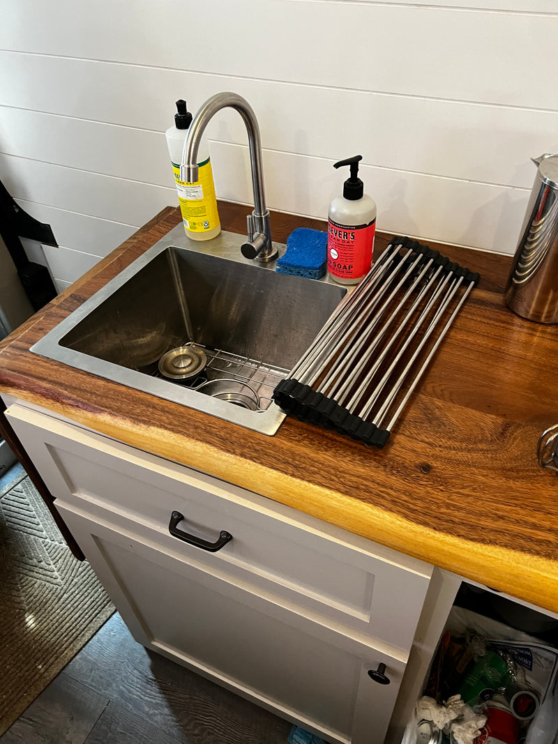 Inside an RV rental, a clean kitchen sink area with a wood counter, soap, and drying rack. — photo 8