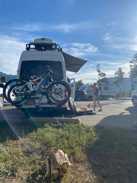 Enjoying an RV rental adventure: white camper van, bikes, and a pet at a scenic lakeside campsite under blue skies.