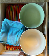 Organized RV rental drawer: green and beige bowls, blue & striped towels. Efficient storage for compact living essentials.