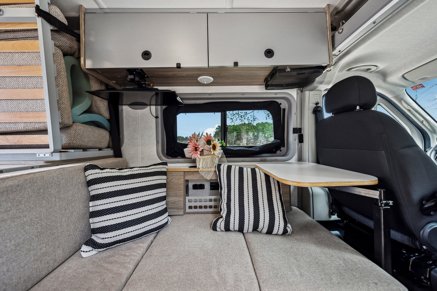 Cozy RV rental interior with convertible seating/bed, smart storage, a movable table, and a scenic window view.