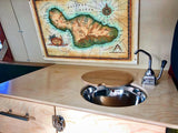Compact RV rental kitchen features a sink with a wooden cover, hand pump faucet, and a large Maui map.