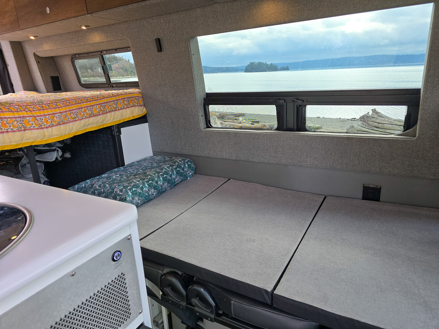 Cozy RV rental interior with a bed, modular seating, and scenic window views of water, islands, and mountains. Perfect for travel. — photo 7