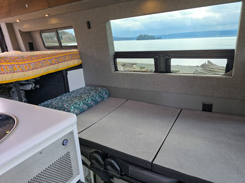 Cozy RV rental interior with a bed, modular seating, and scenic window views of water, islands, and mountains. Perfect for travel. — photo 7