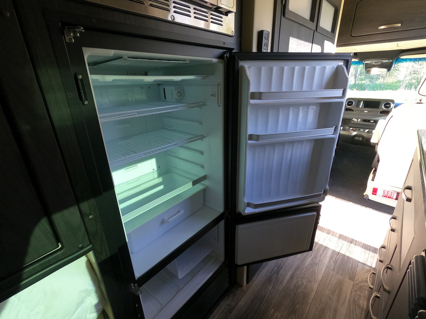 Empty, open two-door refrigerator/freezer inside an RV rental, showing internal shelves and door storage. Ready for your adventure. — photo 10