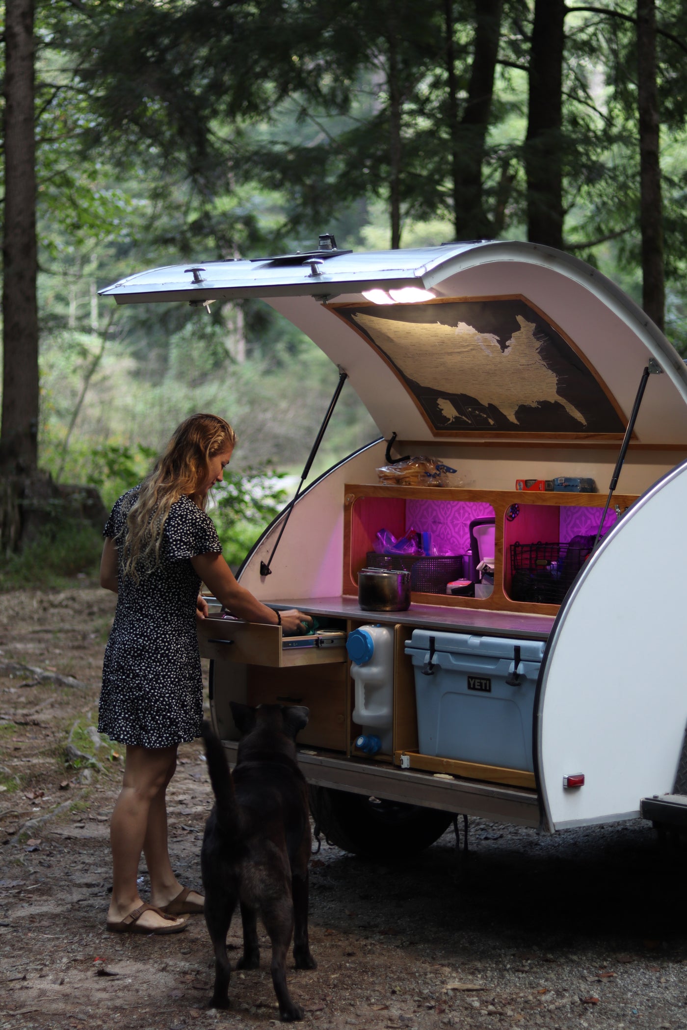 Woman and dog at a compact teardrop RV rental's outdoor kitchen in the forest, perfect for camping. — photo 5