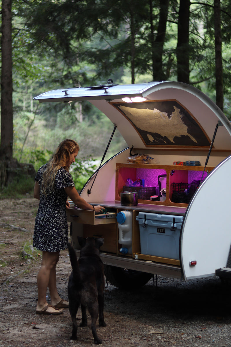 Woman and dog at a compact teardrop RV rental's outdoor kitchen in the forest, perfect for camping. — photo 5