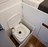 RV rental with a clever space-saving portable toilet integrated into white cabinetry, next to a sleeping area. Ideal for travel.