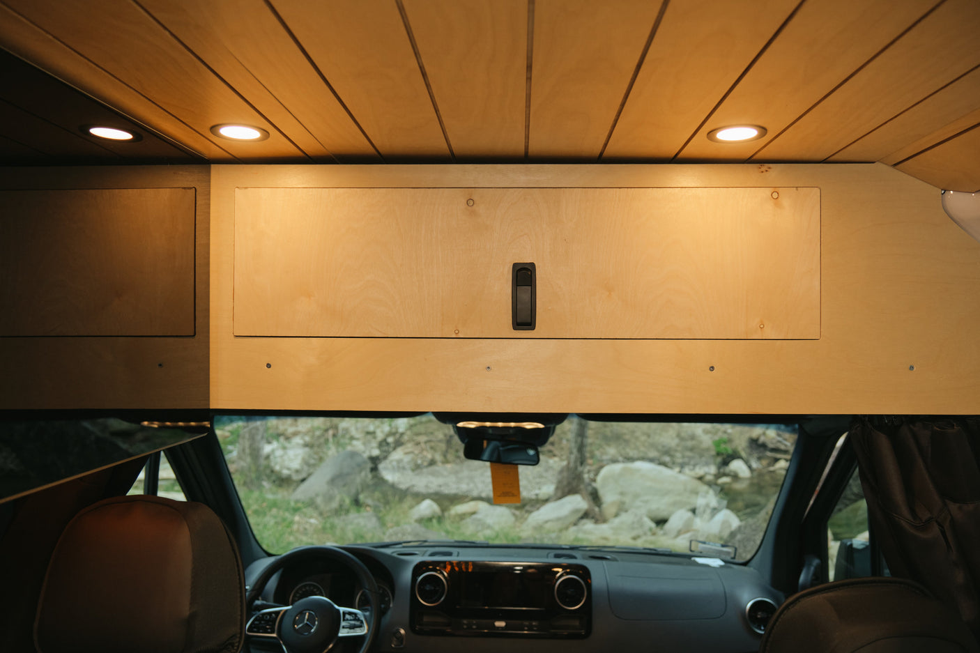 Cozy rv rental camper van interior: wood ceiling & cabinets, LED lights, and a scenic view through the windshield.