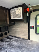 Inside an RV rental: a compact living space featuring a wall-mounted AC, comfortable bedding, and practical cabinetry.