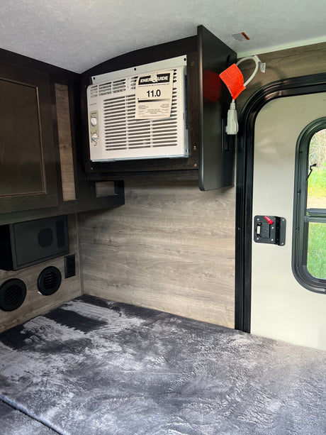 Inside an RV rental: a compact living space featuring a wall-mounted AC, comfortable bedding, and practical cabinetry.