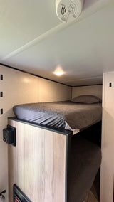Cozy bunk beds in an RV rental, featuring gray quilted bedding, a ceiling light, and a safety detector on the ceiling.