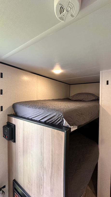 Cozy bunk beds in an RV rental, featuring gray quilted bedding, a ceiling light, and a safety detector on the ceiling.