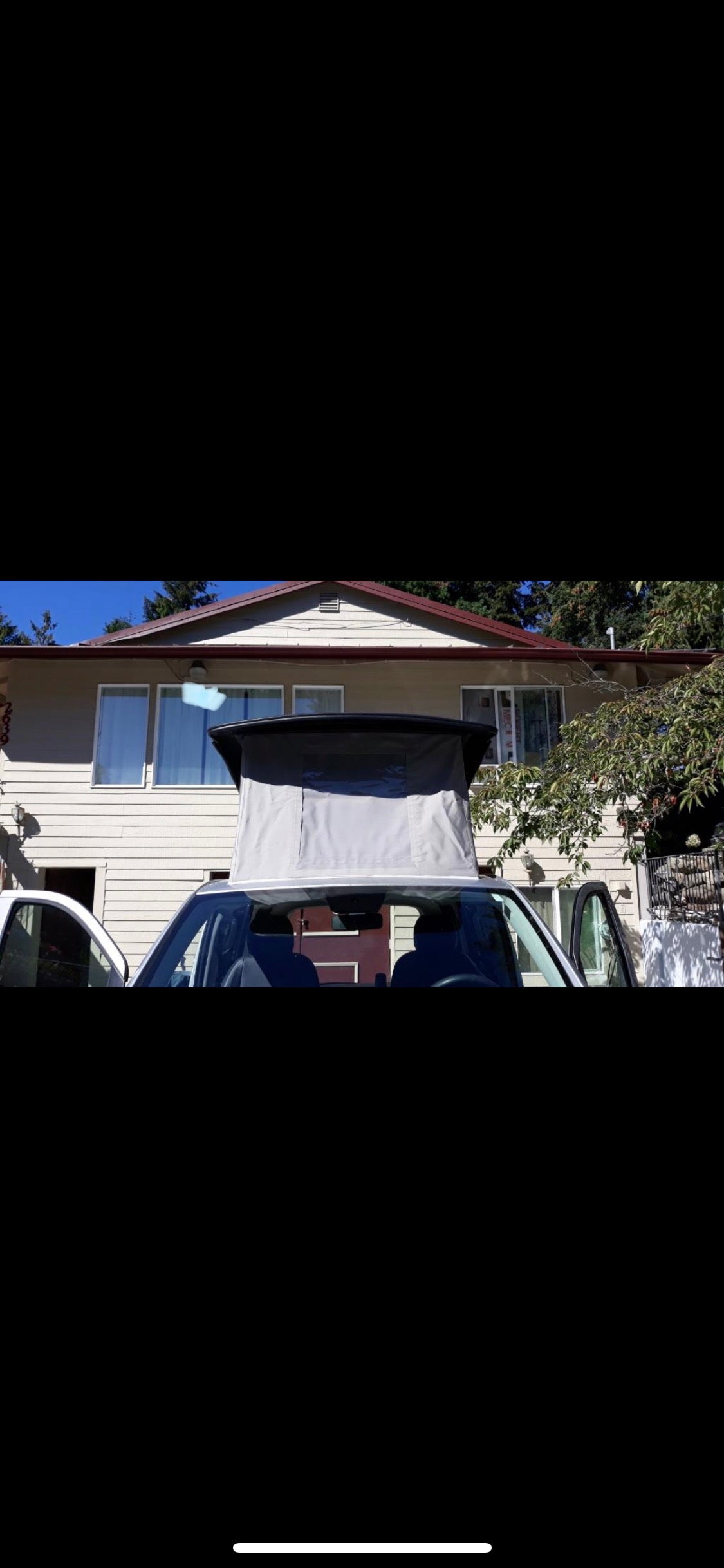 Pop-top camper van RV rental. White van with gray pop-top open, parked at a house on a sunny day. Ready for your adventure.