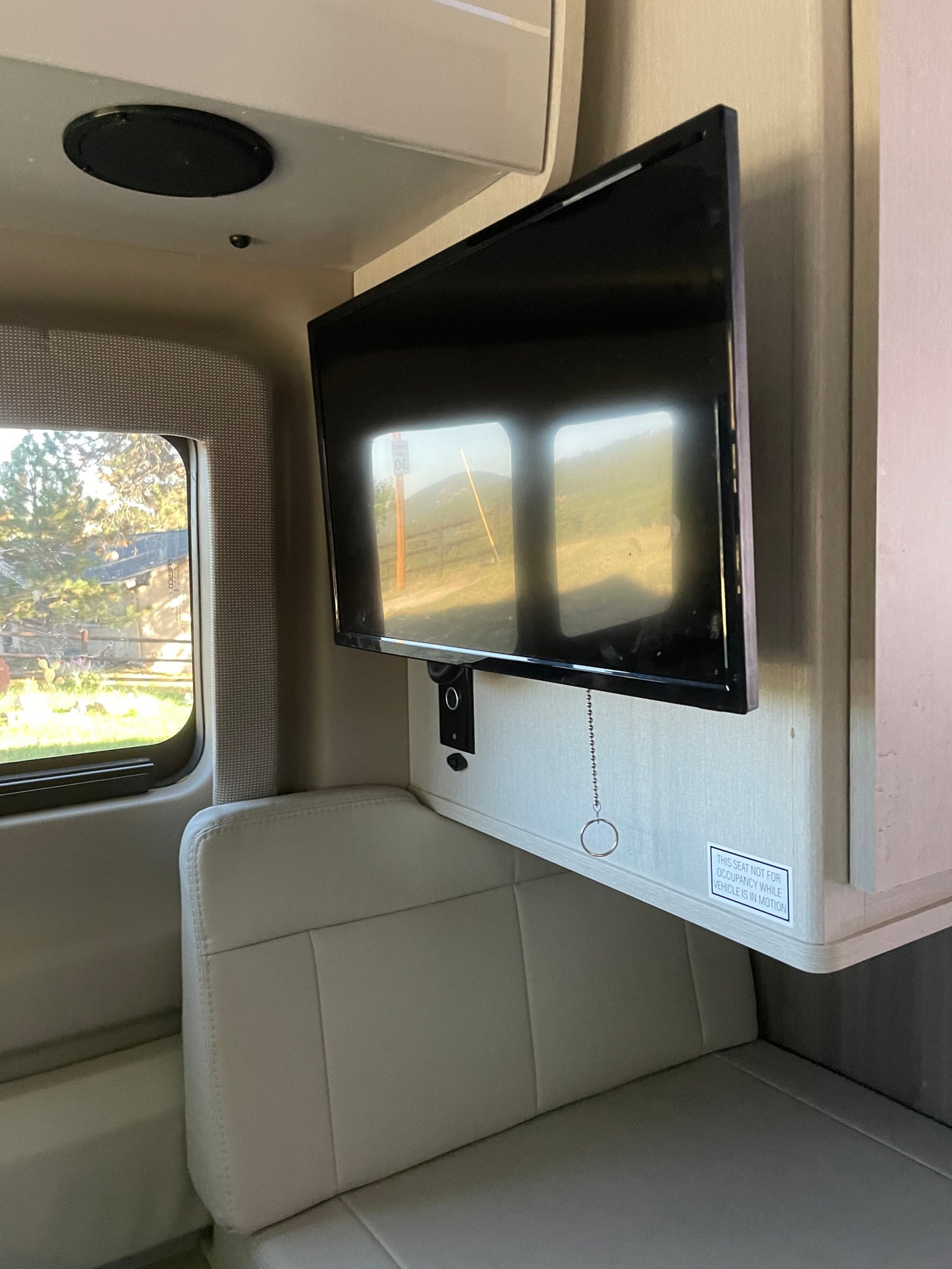 RV rental interior: Mounted TV, comfortable light seating, and a window displaying a scenic outdoor view.