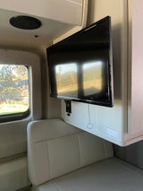 RV rental interior: Mounted TV, comfortable light seating, and a window displaying a scenic outdoor view.