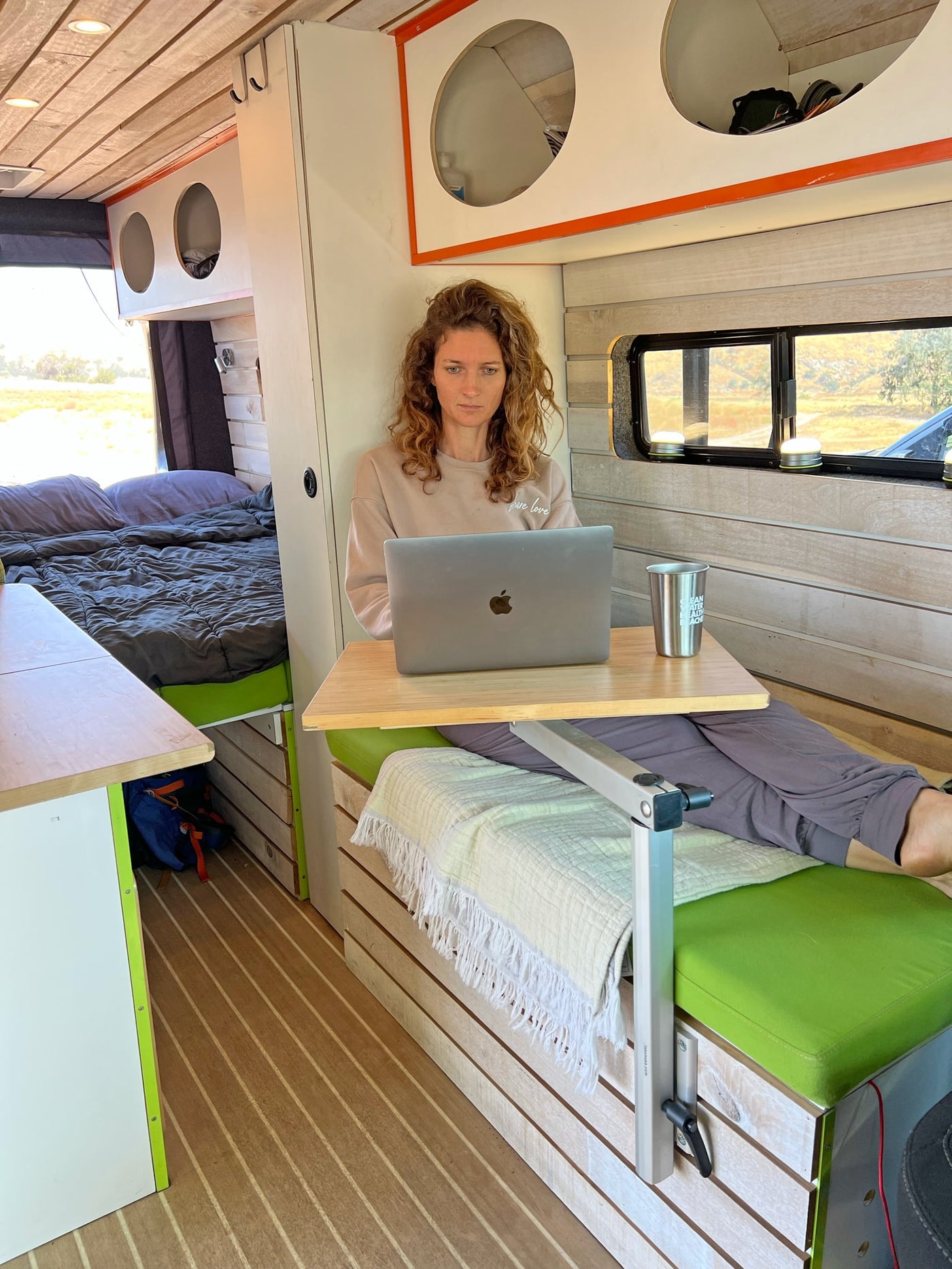  with side door open revealing its custom interior. Parked under trees.|Working remotely from a cozy RV rental: A woman uses her laptop on a bed inside a camper van — photo 9