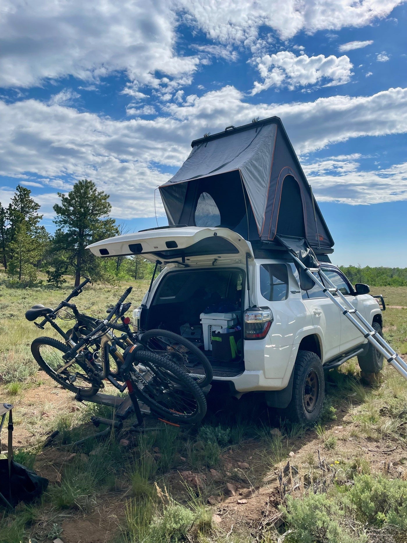 Explore with an RV rental! White SUV, rooftop tent, & mountain bikes set for a wilderness adventure under cloudy skies. — photo 3