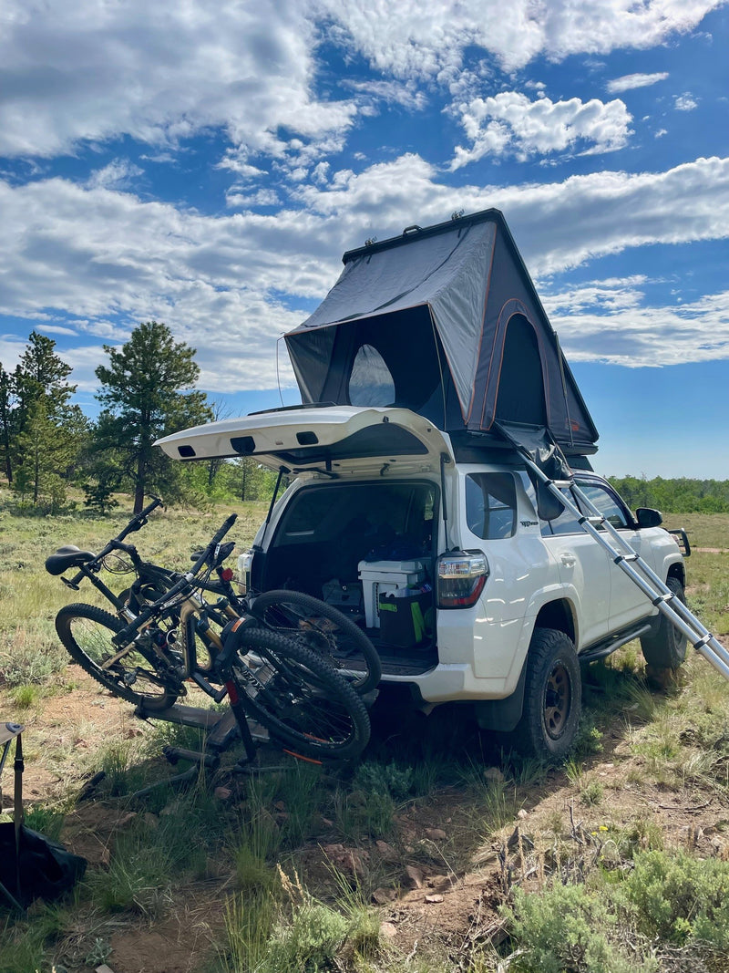 Explore with an RV rental! White SUV, rooftop tent, & mountain bikes set for a wilderness adventure under cloudy skies. — photo 3