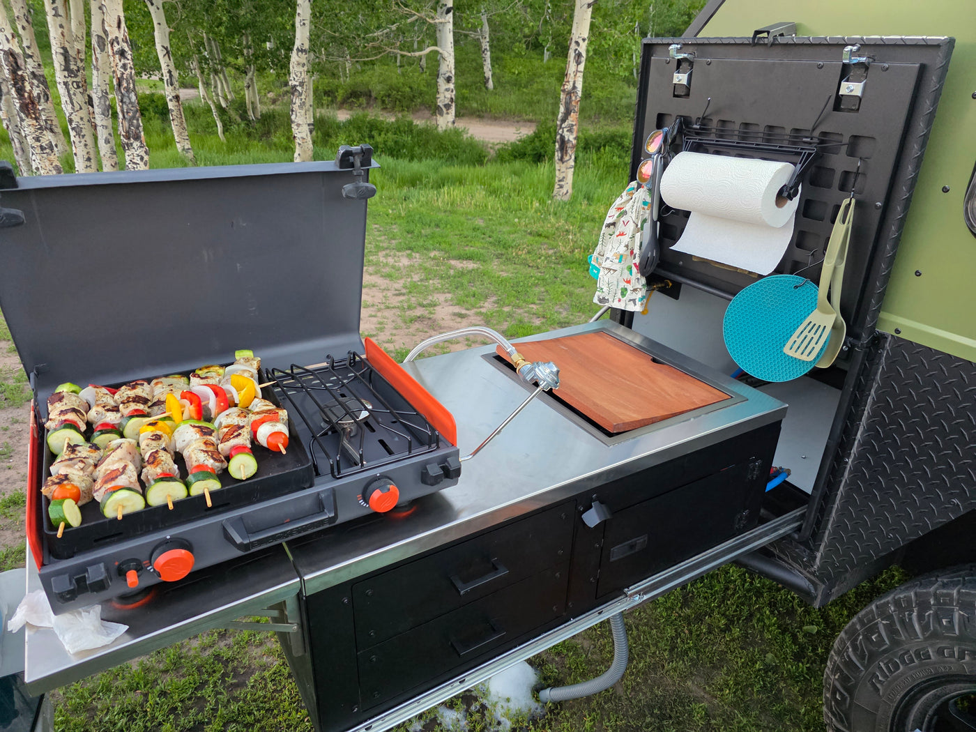 Enjoying an RV rental outdoor kitchen: Kebabs grill on a stove next to a cutting board, paper towels, and cooking tools. — photo 3