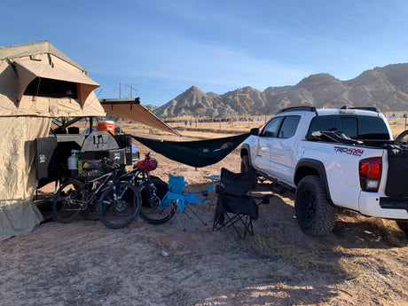 Overland camping: RV rental trailer, truck, bikes, and a hammock setup for off-road adventures and relaxation.