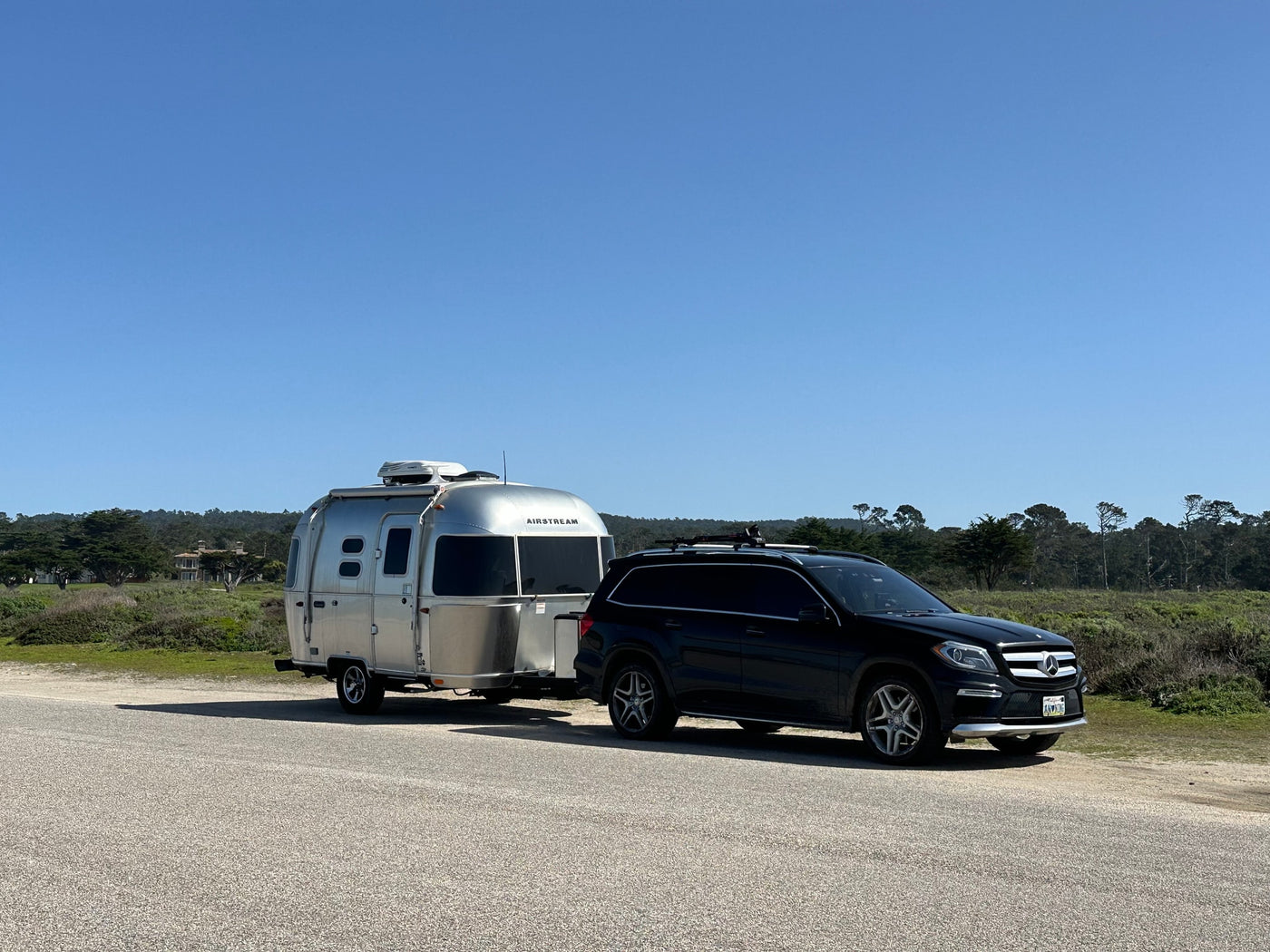 A black Mercedes SUV tows a silver Airstream travel trailer on a sunny day. An ideal RV rental for your next adventure. — photo 4