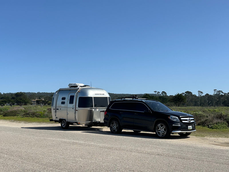 A black Mercedes SUV tows a silver Airstream travel trailer on a sunny day. An ideal RV rental for your next adventure. — photo 4
