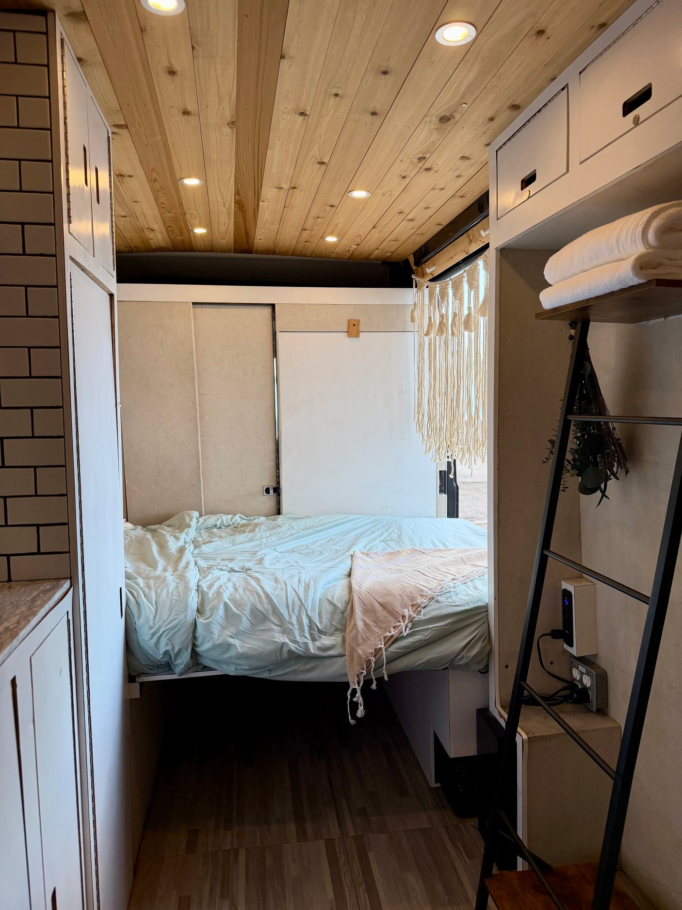 Cozy RV rental bedroom with a comfortable bed, warm wood ceiling with lights, and clever storage solutions for tiny living.