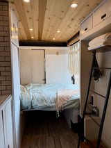 Cozy RV rental bedroom with a comfortable bed, warm wood ceiling with lights, and clever storage solutions for tiny living.