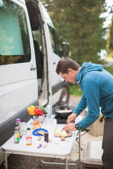 Cooking a fresh meal outdoors with an RV rental. A man preps vegetables by his camper van.