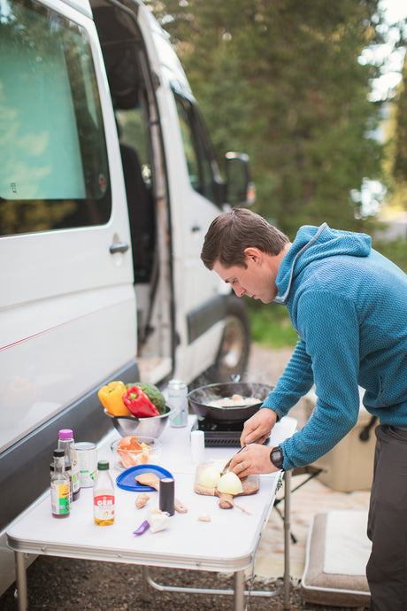 Cooking a fresh meal outdoors with an RV rental. A man preps vegetables by his camper van.