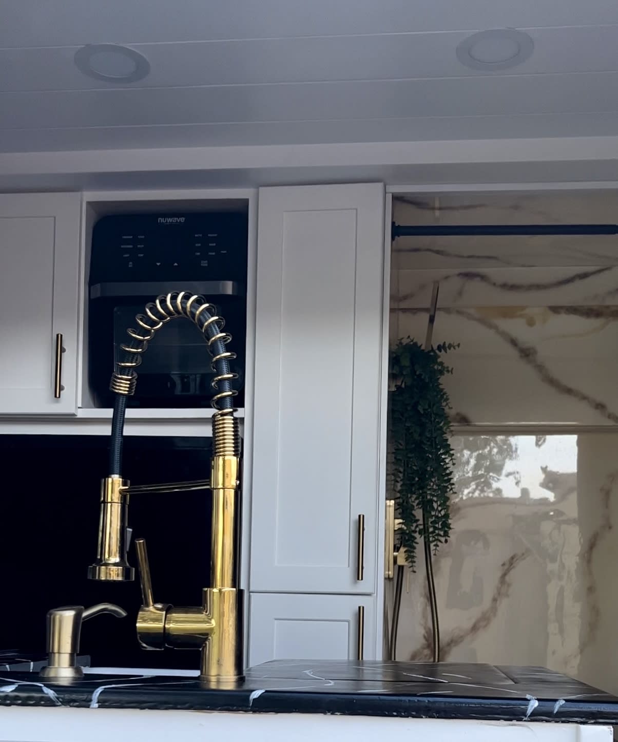 Modern RV rental kitchen: Gold faucet, black marble counter, white cabinets, and built-in Nuwave appliance define this sleek space. — photo 8